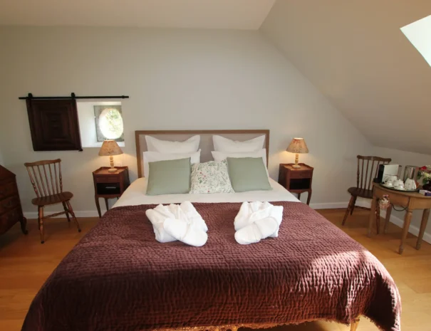 Chambre élégante au Domaine de Champouteau, lit king-size, chaise en bois, commode vintage et serviettes en forme de cygne, ambiance chaleureuse et raffinée