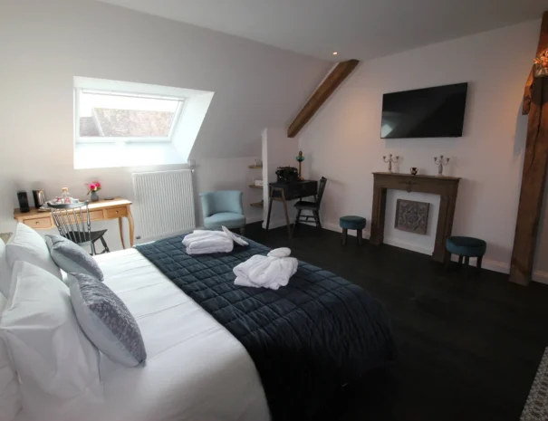 Chambre d’hôtes élégante au Domaine de Champouteau, lit confortable, bureau vintage et cheminée décorative, ambiance chaleureuse et raffinée