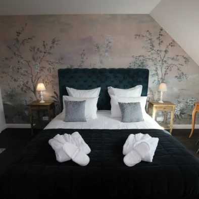Chambre d’hôtes élégante au Domaine de Champouteau, tête de lit capitonnée bleue et mur floral, ambiance romantique et raffinée
