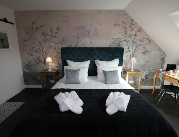 Chambre d’hôtes élégante au Domaine de Champouteau, tête de lit capitonnée bleue et mur floral, ambiance romantique et raffinée
