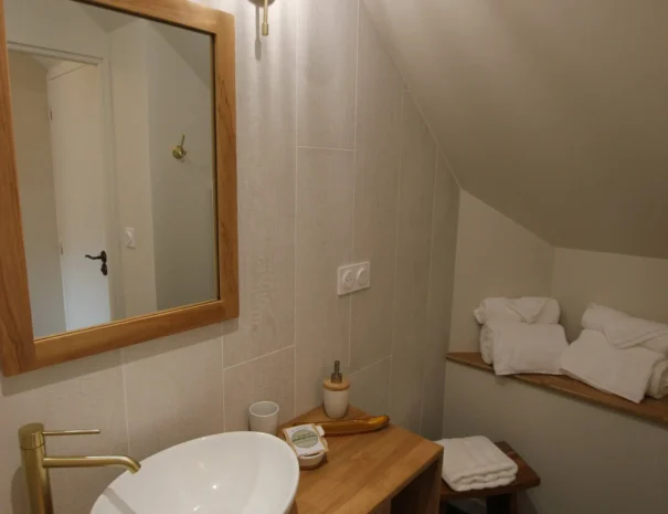 Salle de bain lumineuse au Domaine de Champouteau, lavabo rond sur meuble en bois, miroir et serviette moelleuse, ambiance chaleureuse et apaisante