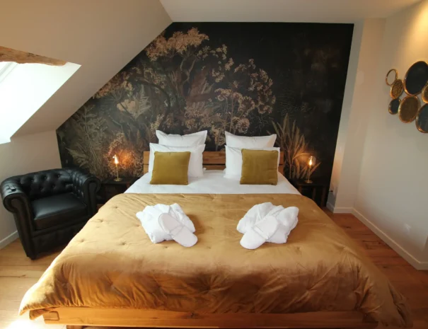 Chambre romantique au Domaine de Champouteau, lit confortable avec serviettes en forme de cygne, fauteuil en cuir et décor floral mural, ambiance chaleureuse et élégante